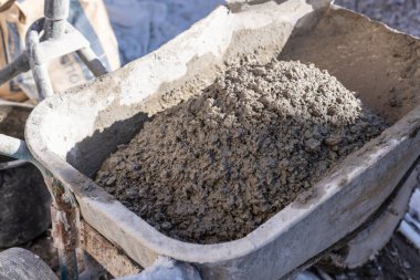 İnşaat alanında çimento karıştırıcıdan el arabasına taze beton dökülüyor. İnşaat ve endüstriyel çalışma kavramı.