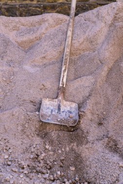 İnşaat kumunun üzerinde duran eski metal kürek. Kumlu dokuda yıpranmış saplı bir kürek resmi. İnşaat ve inşaat alanı kavramı.