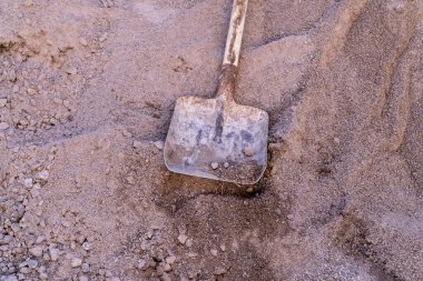 İnşaat kumunun üzerinde duran eski metal kürek. Kumlu dokuda yıpranmış saplı bir kürek resmi. İnşaat ve inşaat alanı kavramı.