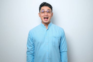 Şaşırmış Asyalı genç adam, ağzı açık, gözleri şişmiş, kameraya bakıyor, izole beyaz arka plan.