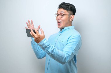 Şok olmuş sıradan gömlekli Asyalı adamın portresi ekranı eğerek cep telefonuyla oyun oynuyor. Vay be yüz ifadesi. Beyaz arkaplanda izole edilmiş resim