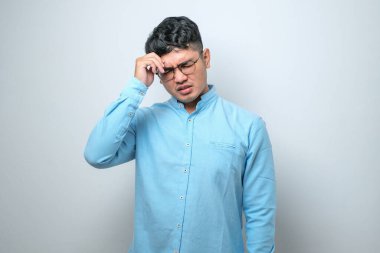 Genç yakışıklı Asyalı adam, günlük gömleğini giyiyor. İzole edilmiş beyaz arka plan üzerinde duruyor. Başı ağrıyor çünkü stres altında. Migren ağrısı..