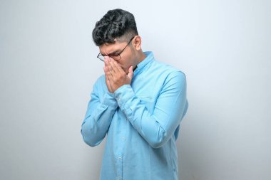 Asyalı genç adam, ağlarken suratını elleriyle kapatan üzgün bir ifadeyle gündelik tişört giyiyor. Beyaz arkaplan üzerinde depresyon kavramı