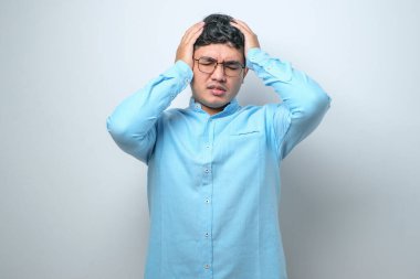Genç yakışıklı Asyalı adam, günlük gömleğini giyiyor. İzole edilmiş beyaz arka plan üzerinde duruyor. Başı ağrıyor çünkü stres altında. Migren ağrısı..
