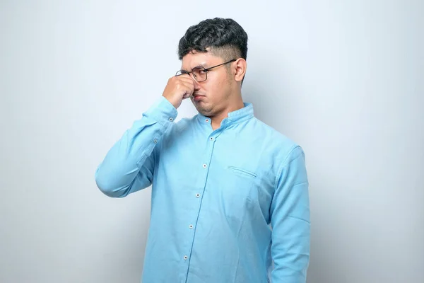 stock image Young asian man wearing casual shirt over white background smelling something stinky and disgusting, intolerable smell, holding breath with fingers on nose. Bad smell