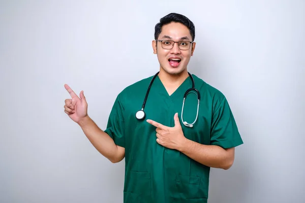 Lachende Knappe Aziatische Arts Verpleegster Scrubs Stethoscoop Wijzende Vingers Linksboven — Stockfoto