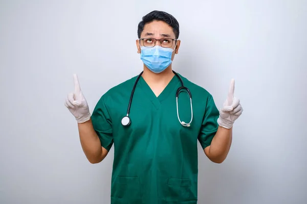緑の頭皮 医療用マスク 指差し指で驚くべきまたは好奇心の強い男性看護師は 患者に白い背景に立つコロナ感染を防ぐ方法を通知します — ストック写真