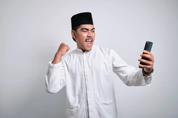 Azji Muzułmanin Człowiek Białych Ubraniach Gospodarstwa Smartfon Robi Zwycięski Gest — Zdjęcie stockowe