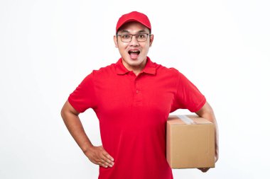 Kırmızı şapkalı ve tişörtlü neşeli Asyalı adam, elinde paket kutusu var. Beyaz arkaplan üzerinde izole nakliye kutusu, istemciden kurye alma paketi