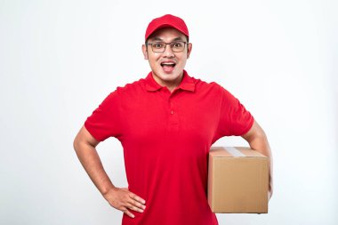 Kırmızı şapkalı ve tişörtlü neşeli Asyalı adam, elinde paket kutusu var. Beyaz arkaplan üzerinde izole nakliye kutusu, istemciden kurye alma paketi