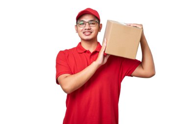 Kırmızı üniformalı gülümseyen Asyalı kurye paketini omuzunda tutuyor, müşteriye siparişlerini beyaz arka planda izole ediyor.