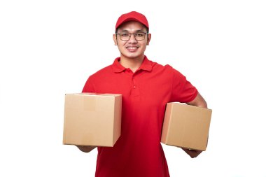 Kırmızı üniformalı gülümseyen Asyalı kurye beyaz arka planda duruyor iki kutu siparişle birlikte, müşteriler için nakliye malzemeleri paketliyor..