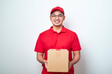 Asyalı genç kurye kırmızı şapkalı ve tişörtlü, izole edilmiş beyaz arka planda duruyor. Önünde karton kutular var. Fotokopi alanı beyaz arka planda izole edilmiş.