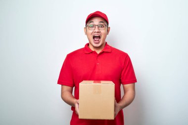  Asyalı genç kurye kırmızı şapkalı ve tişörtlü, izole edilmiş beyaz arka planda duruyor. Önünde karton kutular var. Fotokopi alanı beyaz arka planda izole edilmiş.