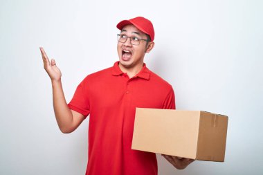 Yakışıklı Asyalı teslimat paketini tutan genç teslimatçı el ve parmak ile beyaz arka planda izole edilmiş sol tarafı işaret ederken şok oldu.