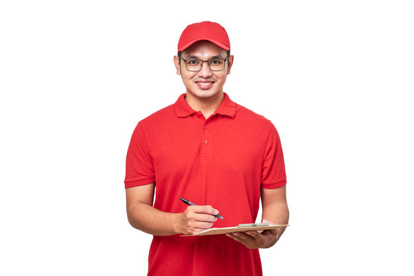 Young smiling asian delivery man in red uniform and cap holding clip board standing on isolated white background.