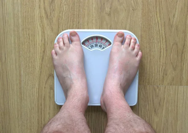 Man\'s weighing himself on bathroom scales