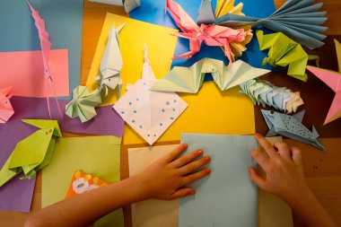 Anaokulu çocuğu renkli kağıtlarla origami hayvanları yapıyor.