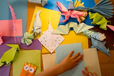 Anaokulu çocuğu renkli kağıtlarla origami hayvanları yapıyor.
