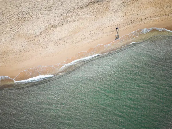 Bir adamın ve köpeğinin havadan görünüşü sahilde huzur içinde yürüyor.