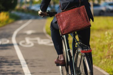 Crop view of anonymous male manager in fashioned suit riding on bike path after work. Elegant executive with expensive leather briefcase getting to work by bicycle on bikeway. Concept of lifestyle.