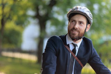 Handsome male businessman in protective helmet commuting at daytime. Portrait of young happy man in stylish suit and tie smiling, while looking around outdoors. Concept of business. 