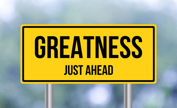 Greatness just ahead road sign on blur background