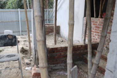 İnşaat alanı, tamamlanmamış tuğla ve bambu iskelesini gündüz ortamına yerleştiriyor, devam eden inşaat süreçlerini gösteriyor.