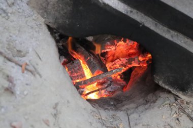 Yakın plan çekimde kuyuda kazılmış turuncu alevler ve yanan odunların gri külleri vardı. Ateş, ısı ve enerji kavramlarını iletir..