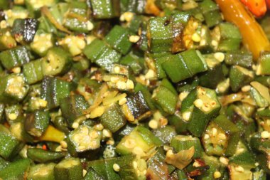 Detaylı bir yakın plan görüntüde kızarmış yeşil bamya dilimleri görünür tohumlarla karıştırılmış, acı biberle süslenmiş, mutfak cazibesini arttıran.