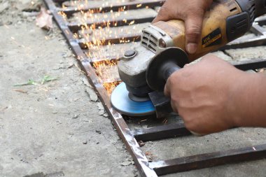 Yakın çekim, Asyalı bir adamı metal bir iskeleti öğütmek için elektrikli bir alet kullanarak, dışarıda çalışırken kıvılcımlar üretirken yakalıyor..