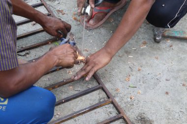 Yakın plan çekimde, metal kaynak yapan Hintli zanaatkarları yakalıyor, kıvılcımlar uçuşuyor. Eller pense, el işi, beceri ve açık havada günlük kıyafet kullanır..
