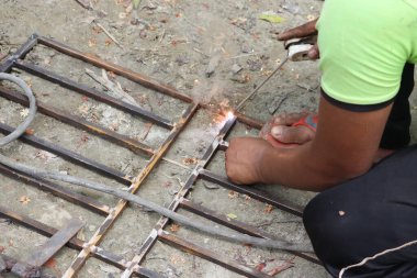 Yakın plan, kaynak çubuklarını kullanarak, kıvılcımlar, gösterişli işçilik ve metal işçiliğiyle vurgulanmış, siyah derili bir kaynakçıyı yakalıyor..