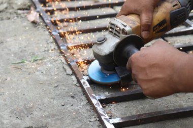 Metal çerçevedeki pürüzsüz kaynak eklemleri için insanın elleri metali öğütür, kıvılcımlar uçuşur. Detaylı el hareketlerini ve öğütme hareketlerini gösteren yakın çekim.