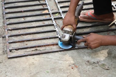 Adam dışarıda çalışıyor. Açı öğütücüsünü kullanarak metal şebekeyi kesiyor, kıvılcım saçıyor. Gerçek bir açık hava ortamında güç aracını kullanmaya odaklanmış.