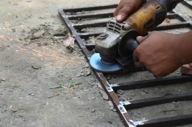 Koyu tenli eller metale karşı bir elektrikli alet tutuyor ve havaya kıvılcımlar yolluyor. Çerçeve kumlu bir yüzey üzerinde otururken araç hareket ile bulanıklaşır.