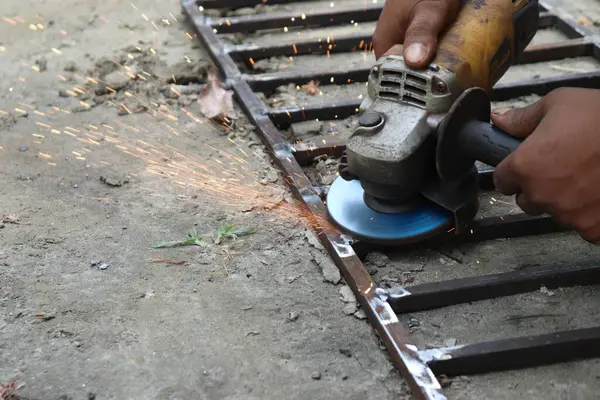 Metali dairesel bir testereyle öğüten etnik işçilerin elleri çimentoda parlak kıvılcımlar oluşturuyor. Açı öğütücüsünün eylem halindeki görünümü.