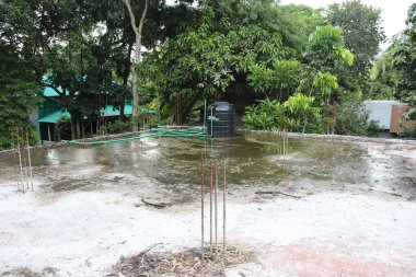 Görüntü su tankını, yeşil boruları, metal çubuklu binaları, yeşil yaprakların altındaki çatıyı gösteriyor. Açık havada, gündüz vakti..