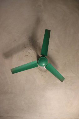 Üç pervaneli yeşil tavan vantilatörüne bakıyorum, beyaz bir tavana monte edilmiş, loş bir gölge bırakıyor..