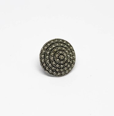 Yakın çekim, dairesel metal bir halka sergiliyor. Küçük noktalardan oluşan karmaşık bir desen içeriyor. Temiz, parlak beyaz bir yüzeyde sunuluyor, detaylarını geliştiriyor..