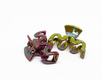 Yakın planda, biri başta pembe diğeri altın olmak üzere iki yanardöner saç tokası sergileniyor. Pürüzsüz beyaz bir arkaplan ile çevrelenmiş, pürüzsüzlüklerini vurguluyorlar..