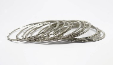 Geleneksel Hint bilekliklerinde yığılmış metal bilezikler. Beyaz arka plana karşı boncuklu ve çarpık tasarımlı gümüş bilezikler..