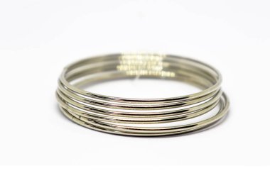 Yakından çekilen bir yığın metalik gümüş bilezik, ışığı yansıtan, düz beyaz zemin ile zıt.