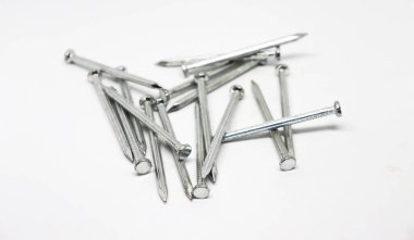 Yakın çekim, düz başlı ve sivri uçlu gümüş renkli metal çivilerden oluşan bir yığın içeriyor, temiz beyaz bir yüzeye rastgele dağılmış..