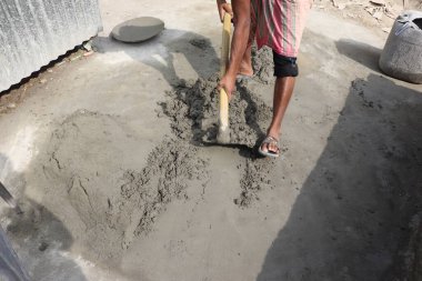 Geleneksel giysiler giymiş, kürek takmış, çimentoyu dışarıda gündüz vakti karıştıran kimliği belirsiz birinin gövdesi..