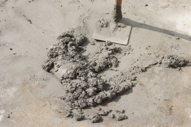 Yüzeyde taze çimento ve kürek var, zemin çalışması ve ev yapımı projeler için uygun..