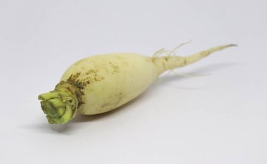 Hafif kirli, kesilmemiş bir daikon turp düz beyaz bir arkaplan önünde yatay olarak sergilenir. Daikon 'un renkleri sarı ile yeşil ve beyaz arasında değişir..