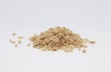 Düz beyaz arka planda, kırmızı renkte benekli bej pirinç taneleri sergilenir. Üssün dört bir yanına dağılmış tahıllar görsel bir ilgi yaratıyor..