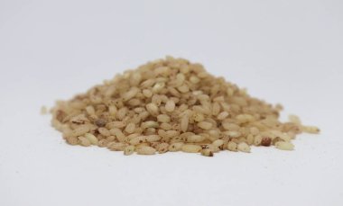 Görüntü, bej pirinç taneciklerinin doğal dokularını vurgulamak için düz ve parlak bir nötr yüzeyde sergilenen küçük bir tepeciği gösteriyor..