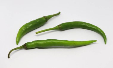 Parlak beyaz bir ortama karşı izole edilmiş resimde, şekil ve boyutta doğal varyasyonları gösteren üç taze, canlı yeşil biber, mutfak ve yemek fotoğrafçılığı yer alıyor..